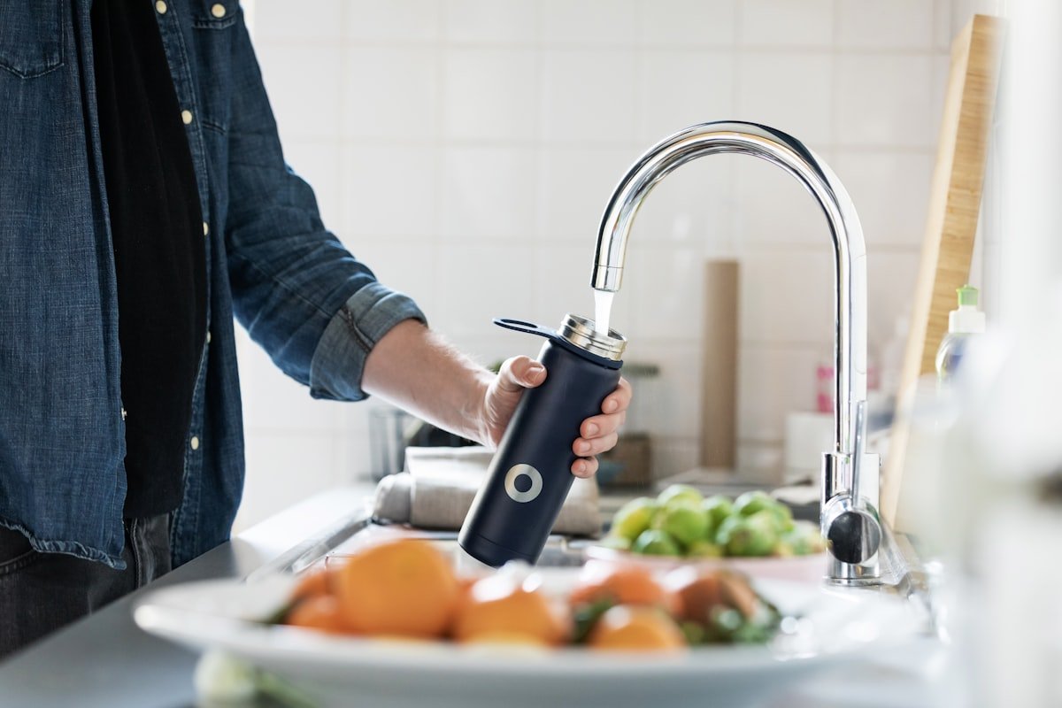 Person filling water bottle at kitchen faucet representing spring plumbing maintenance for Spring TX homeowners